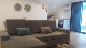 A modern living room with a sectional sofa, a small round coffee table, and a kitchen in the background. - Maria's House (Câmara de Lobos)