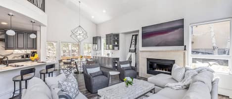 A spacious living room with a fireplace, grey sofas, and a dining area with a large window.