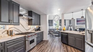 A modern kitchen with dark cabinets, a stainless steel stove, and a dining area with a glass table and chairs. - 4 Bedroom Luxury Home in East Vail (Vail)