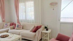 Uma sala de estar aconchegante com um sofá bege, uma mesa pequena branca e uma poltrona rosa.