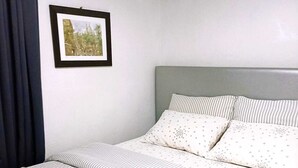 A neatly made bed with striped bedding and pillows, a framed picture on the wall, and a folded white towel on the bed.