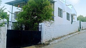 Um edifício branco com telhado metálico, um portão preto e uma árvore à frente.