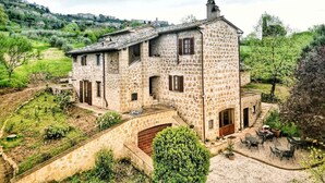 Une maison en pierre avec une cour, un escalier menant à l’entrée et une vue sur la campagne environnante.