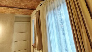 Une pièce avec un plafond en pente, un radiateur, une armoire blanche et une fenêtre avec des rideaux.