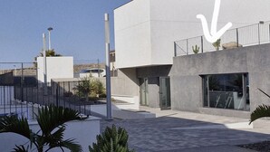 Een modern gebouw met een plat dak, een schotelantenne en een omheinde binnentuin met cactussen en palmplanten.