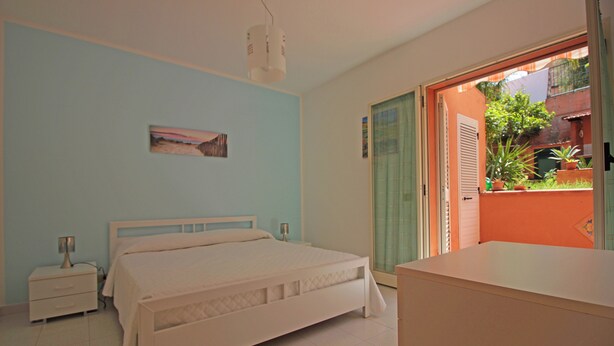 A bedroom with a bed, bedside tables, a nightstand, a window with a view of the outside, and a door leading to a balcony. - Villetta Santa Lucia con patio e giardino by Wonderful Italy (Cefalù)