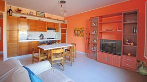 A modern kitchen with wooden cabinets, a dining table, and chairs. There is a sofa in the living area. - Villetta Santa Lucia con patio e giardino by Wonderful Italy (Cefalù)
