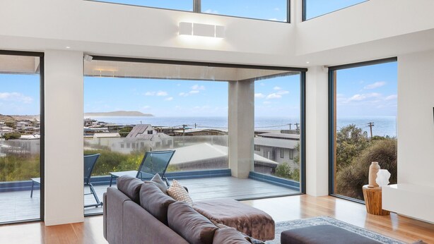 Ein modernes Wohnzimmer mit einem großen Glasfenster, das auf einen Balkon mit Meerblick führt.
