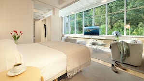 A modern hotel room with a large bed, a TV, a sofa, and a view of the outdoors.