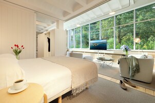 Habitación de hotel moderna con una cama grande, televisor, sofá y vistas al exterior.