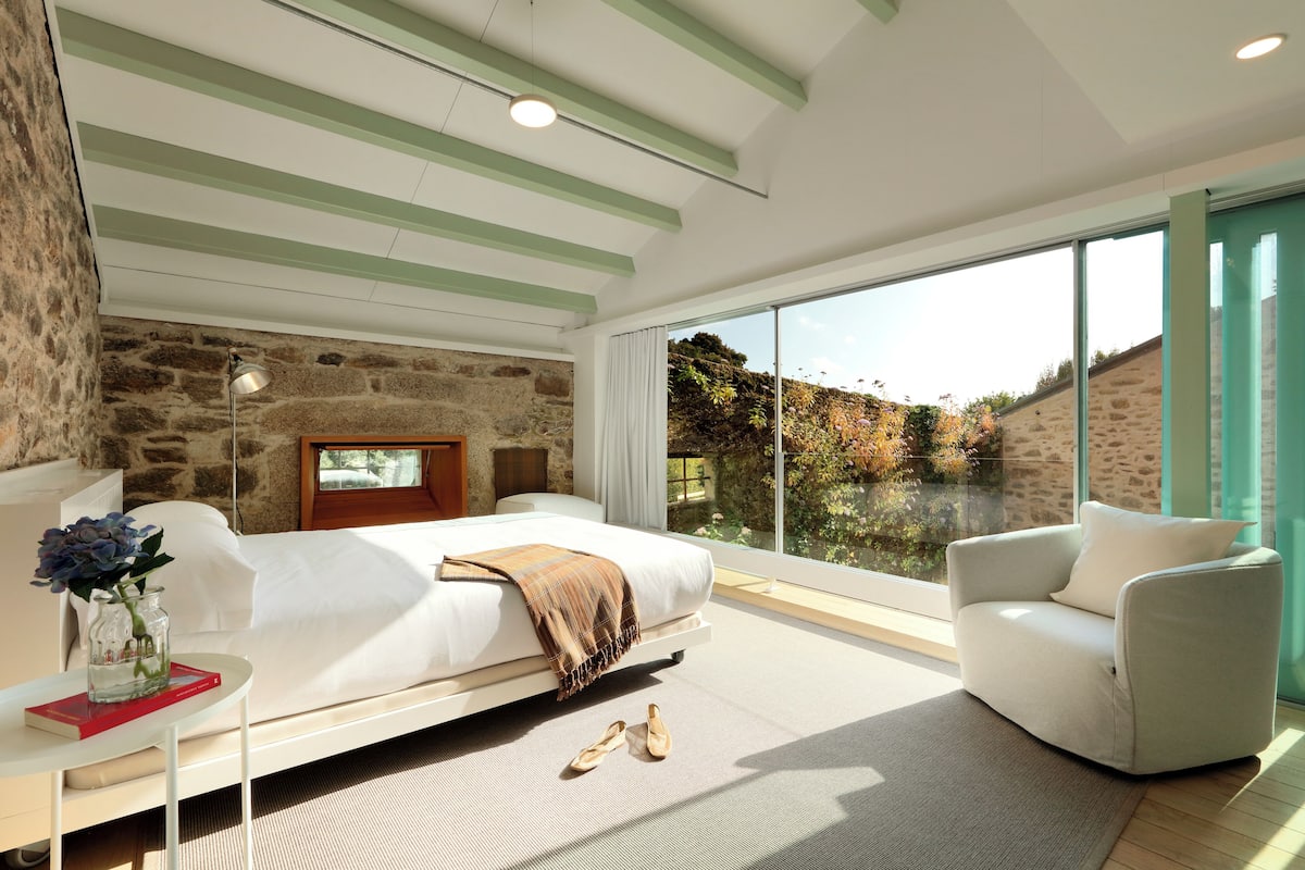 Une chambre moderne avec un grand lit, un canapé et une vue sur un mur de pierre et la verdure environnante.