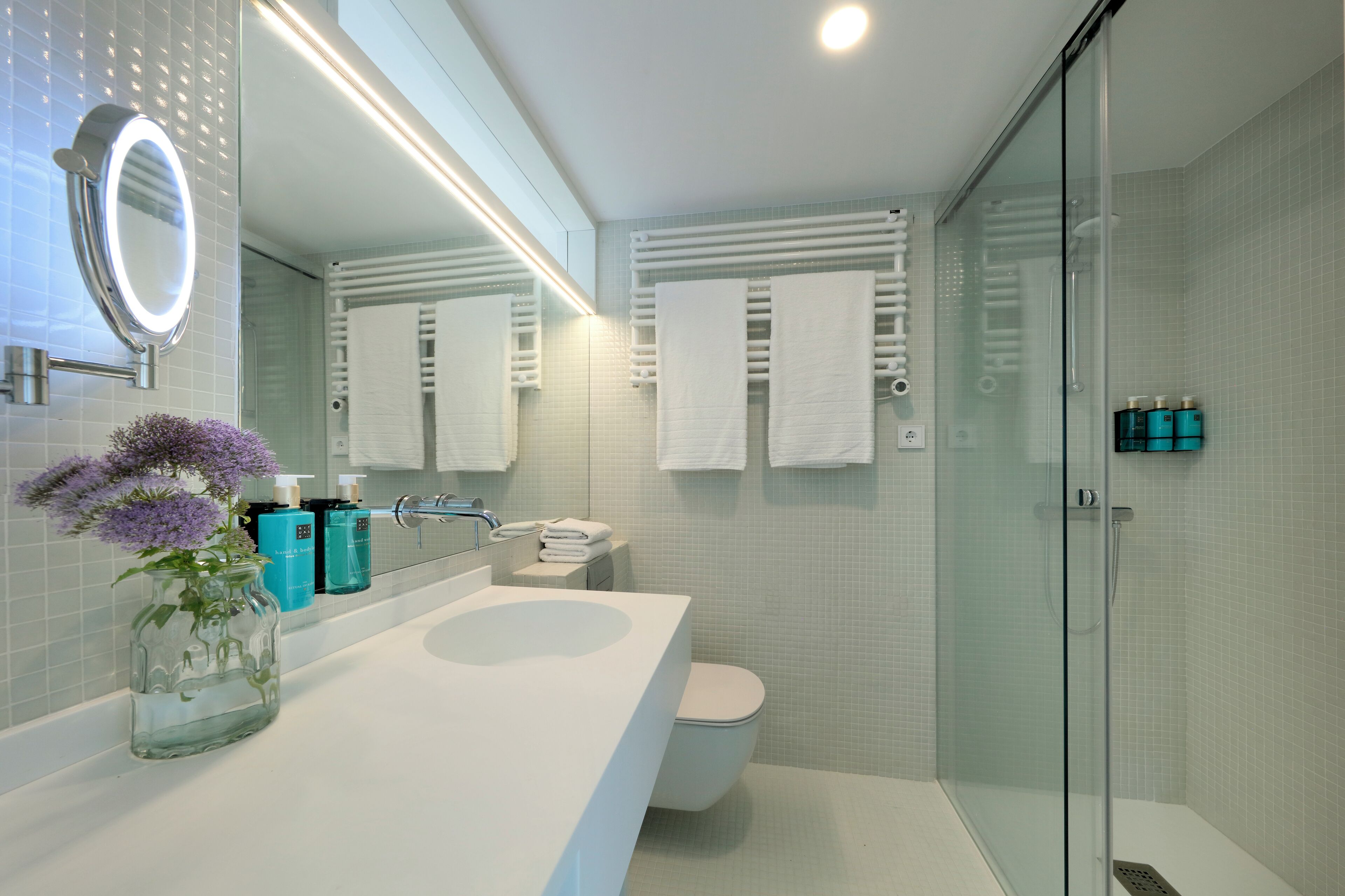 A modern bathroom with a glass shower enclosure, a white sink, and a large mirror.