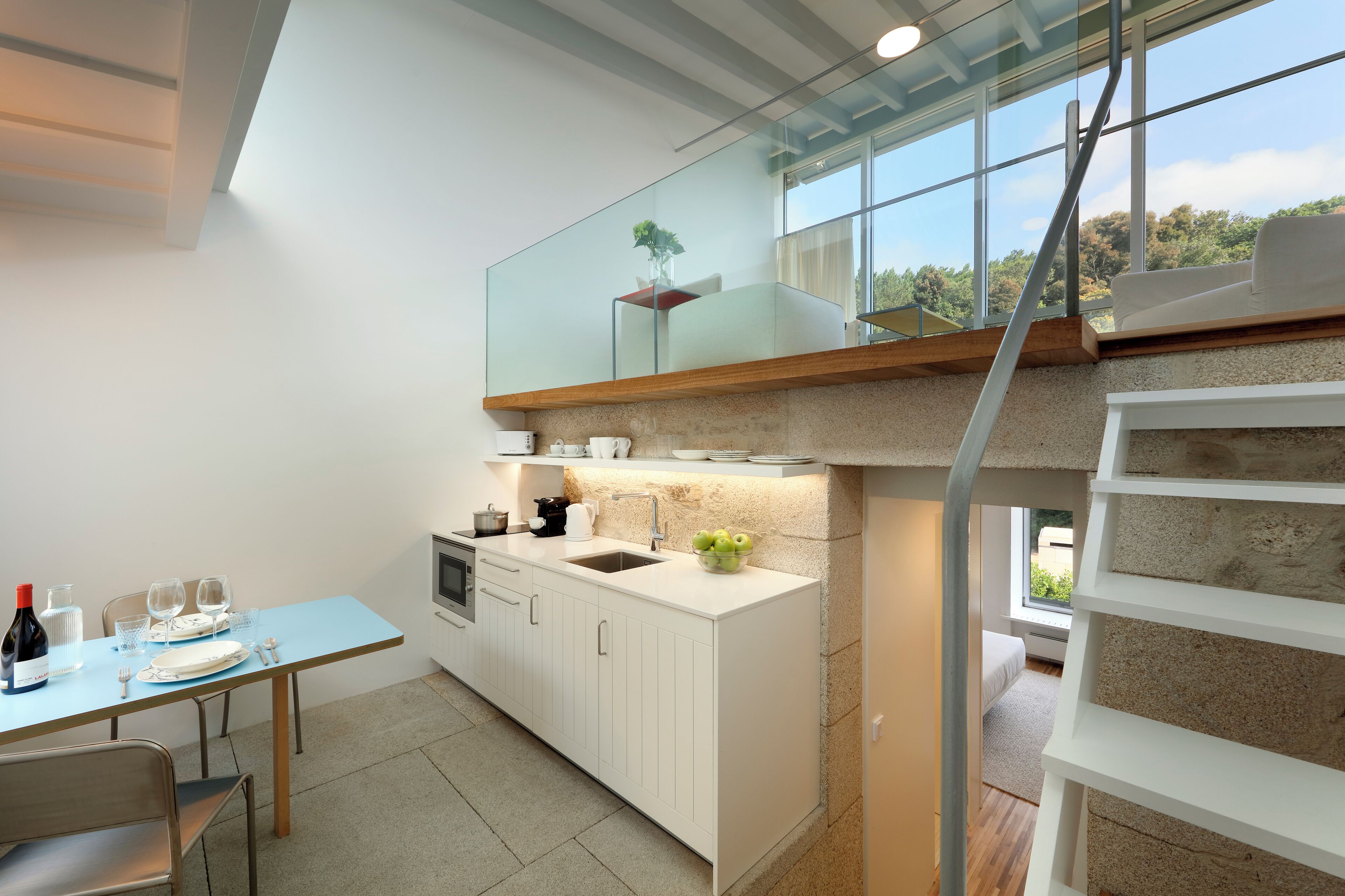 Una cocina moderna con comedor, una escalera y vistas al exterior con vegetación.