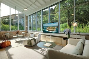 Un salón moderno con amplios ventanales, televisor de pantalla plana, asientos cómodos y vistas a zonas verdes.