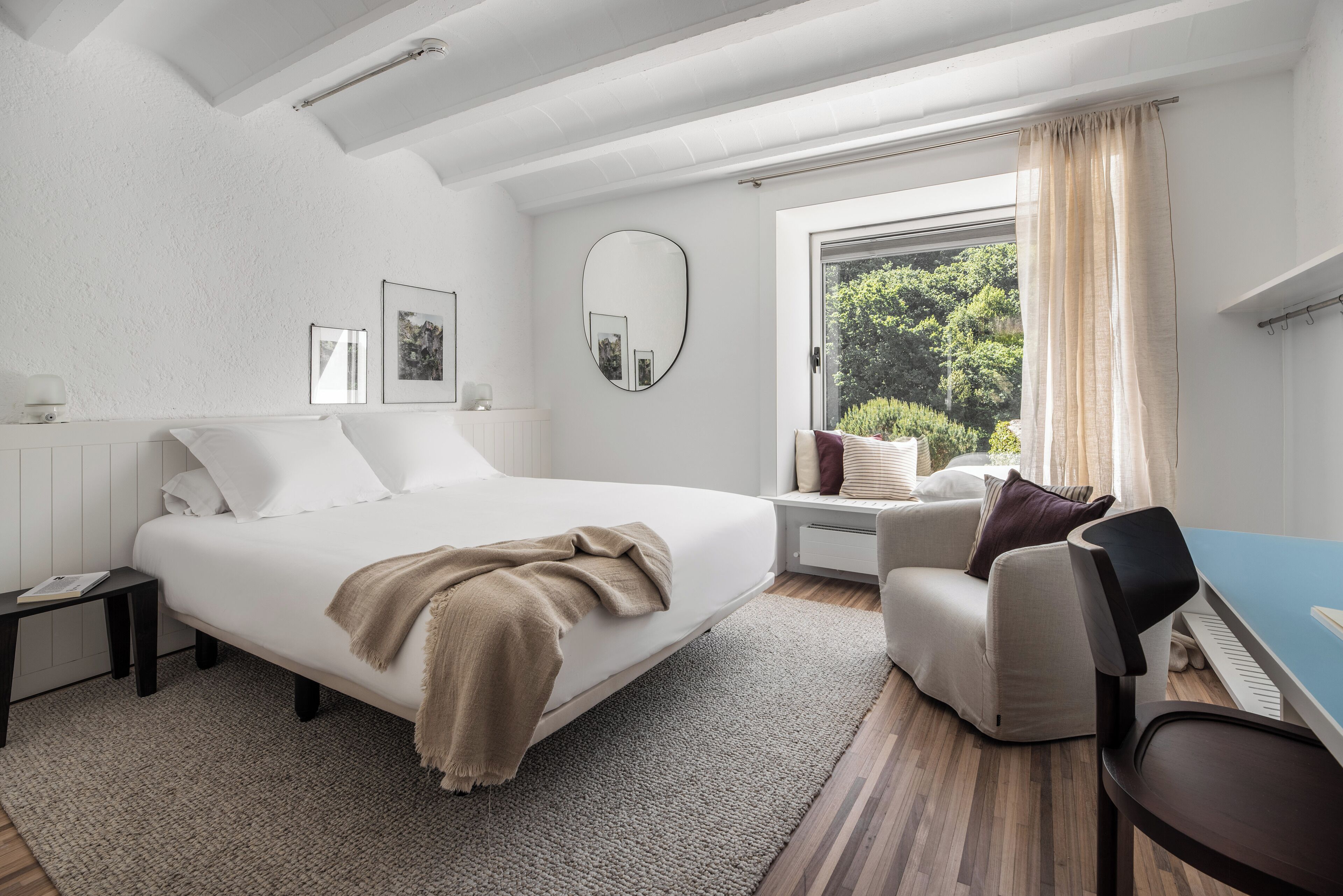 A modern bedroom with a large bed, a desk, a chair, and a window with curtains.