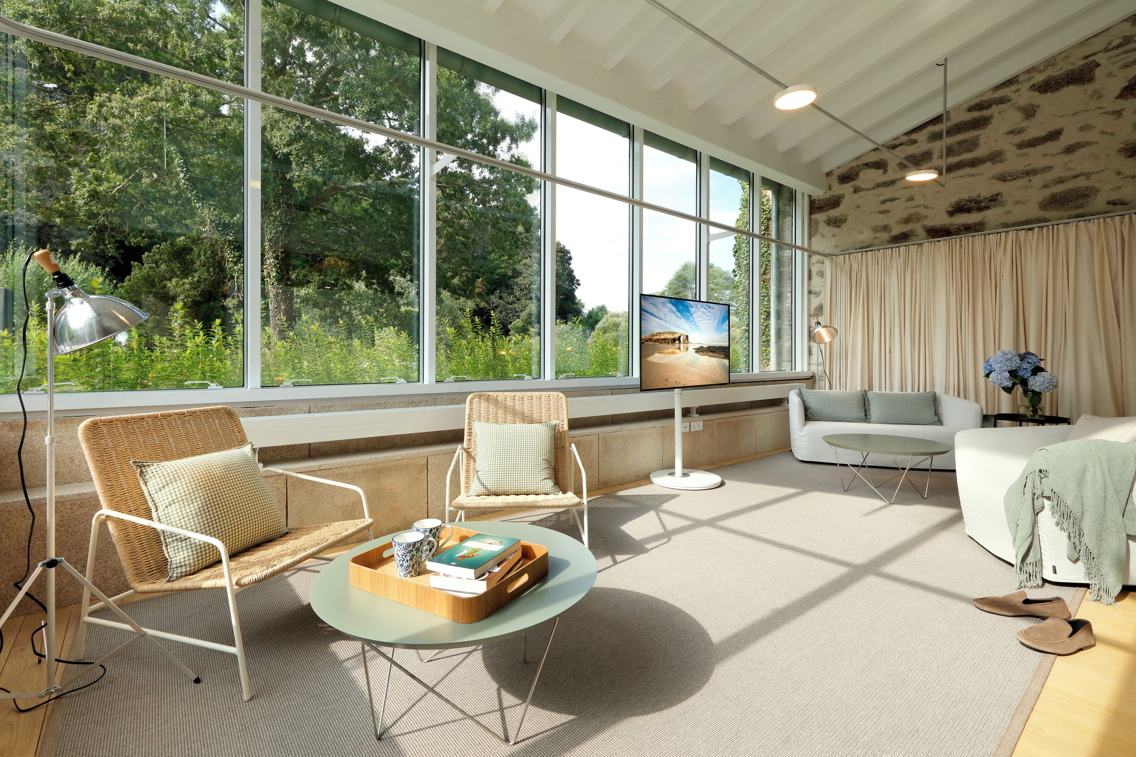 A spacious living room with large windows, a sofa, two armchairs, a coffee table, and a television.