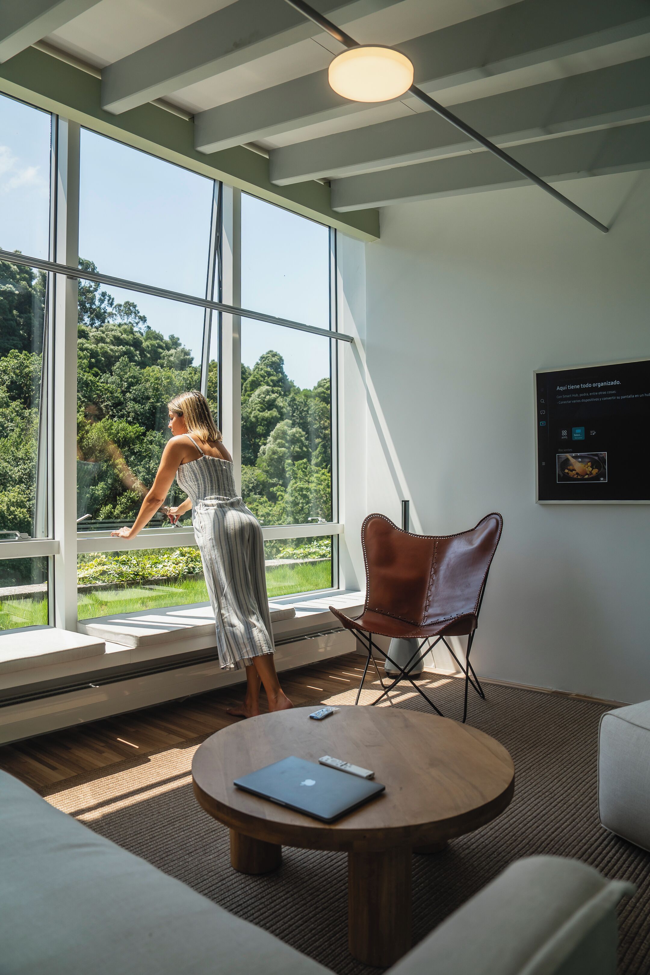 Ein modernes Interieur mit großen Fenstern, einem Ledersessel, einem runden Holztisch und einem Laptop.