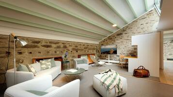 Ein modernes Wohnzimmer mit Steinwand, weißen Möbeln, einem Flachbildfernseher und einem großen Fenster.