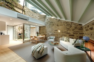 Una sala de estar moderna con una pared de piedra, un ventanal que da a un área exterior y una acogedora disposición de asientos.