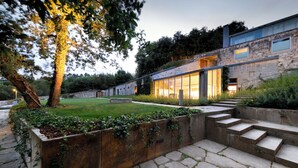 A modern house with a stone facade, large windows, and a well-maintained garden with steps leading to the entrance.