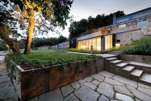 Una casa moderna con fachada de piedra, ventanas amplias y un jardín cuidado con escalones que conducen a la entrada.