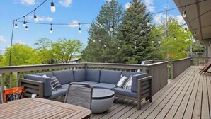 A wooden deck with a built-in seating area, string lights, and a view of trees.