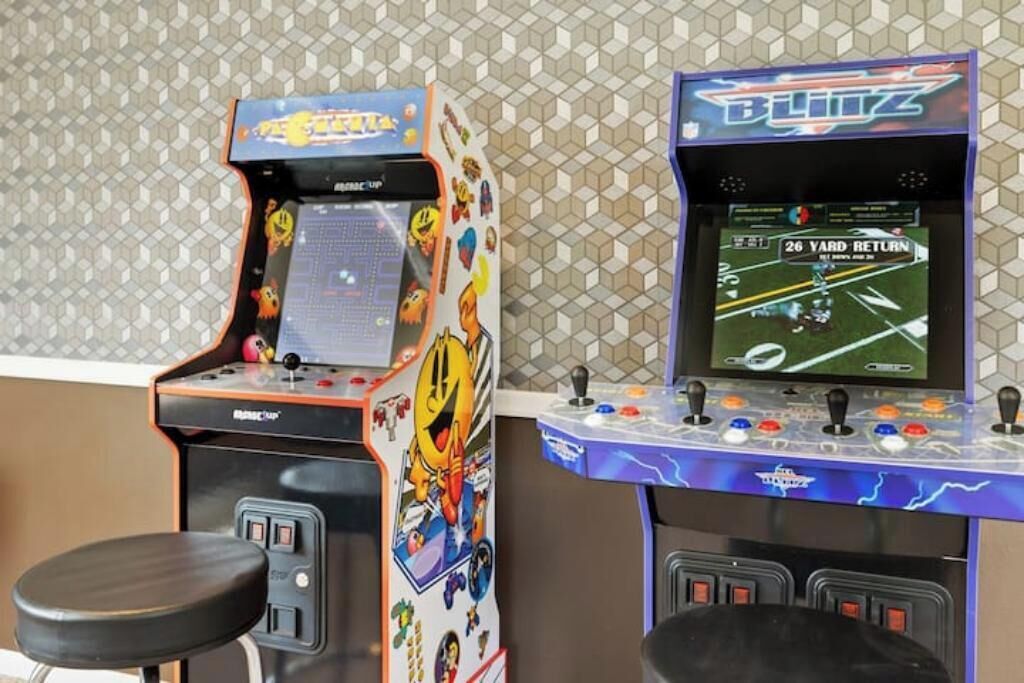 Deux bornes d’arcade, l’une portant l’inscription « Blitz » et l’autre « Racing Champ », avec un mur à motifs en arrière-plan.