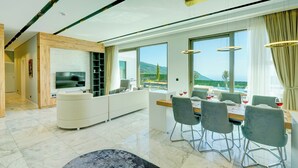 A modern living room with a large TV, a dining area with a table set for four, and a view of the mountains through large windows. - Pluto-1 PLANET LUXURY VILLAS (Kas)