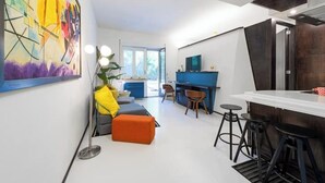 A modern living room with a sofa, ottoman, and bar area with stools. There is a large painting on the wall and a window providing natural light. - The House Suite Sorrento in Corso Italia  (Sorrento)