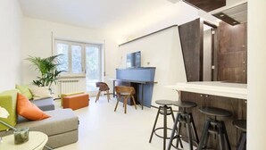 A modern living room with a sofa, chairs, a small table, and a kitchen area with stools. - The House Suite Sorrento in Corso Italia  (Sorrento)