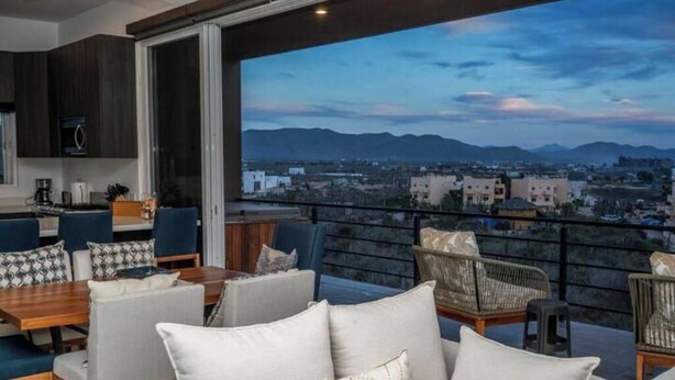 A balcony with a city view, dining area with chairs and tables, and a kitchen area with cabinets and appliances. - Quick walk to Cerritos Beach, private Hot tub, pool, gym, ocean & mountain VIEWS (Los Cerritos)