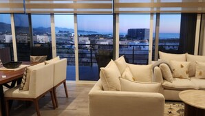 A modern living room with a large window offering a city view, a sofa set, a dining table, and a small round table. - Quick walk to Cerritos Beach, private Hot tub, pool, gym, ocean & mountain VIEWS (Los Cerritos)