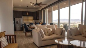 A modern living room with a sofa set, a dining area, and a kitchen. There is a large window providing a view of the cityscape. - Quick walk to Cerritos Beach, private Hot tub, pool, gym, ocean & mountain VIEWS (Los Cerritos)