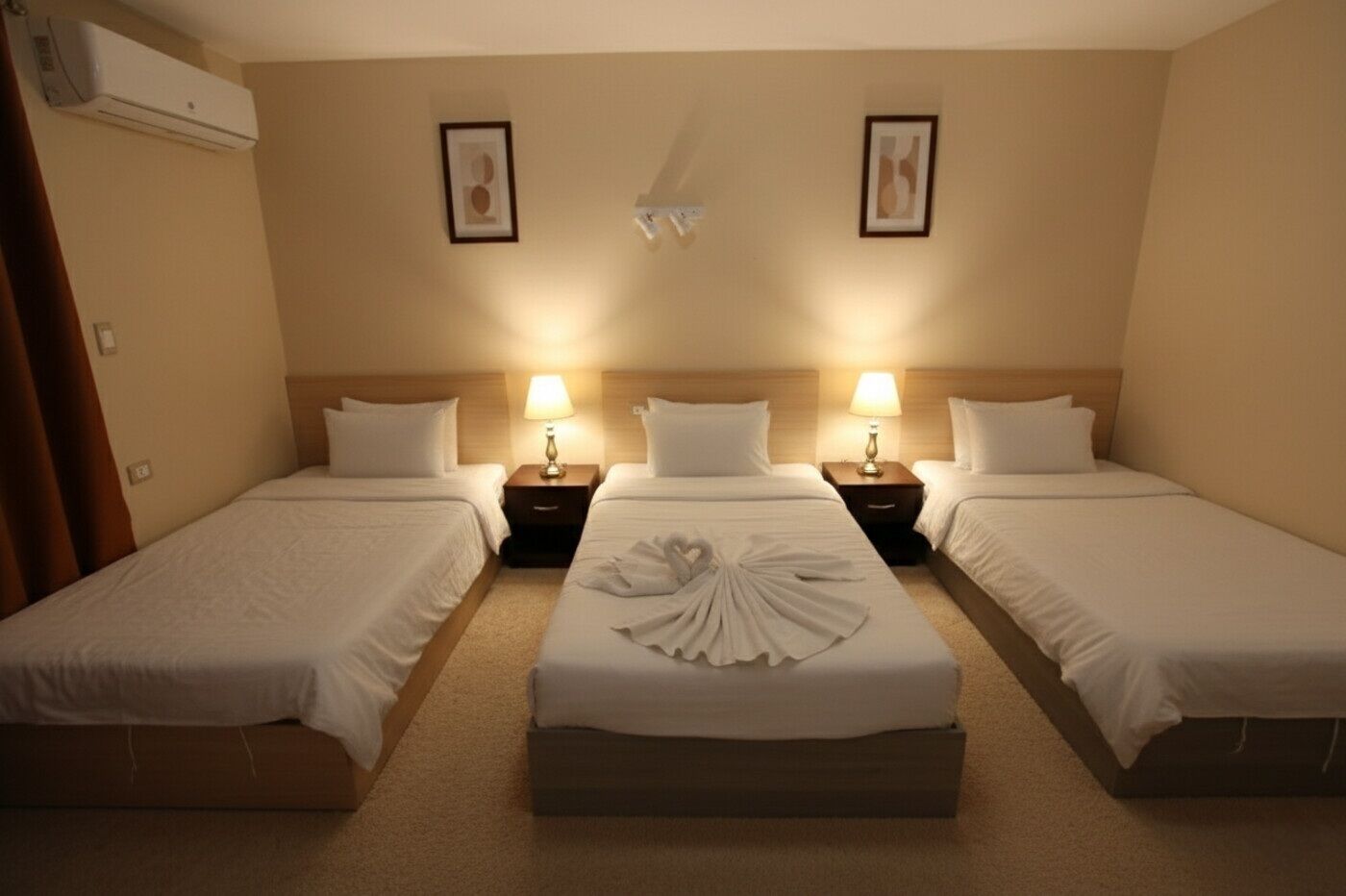 Habitación de hotel con tres camas individuales, cada una con una mesita de noche y lámpara.