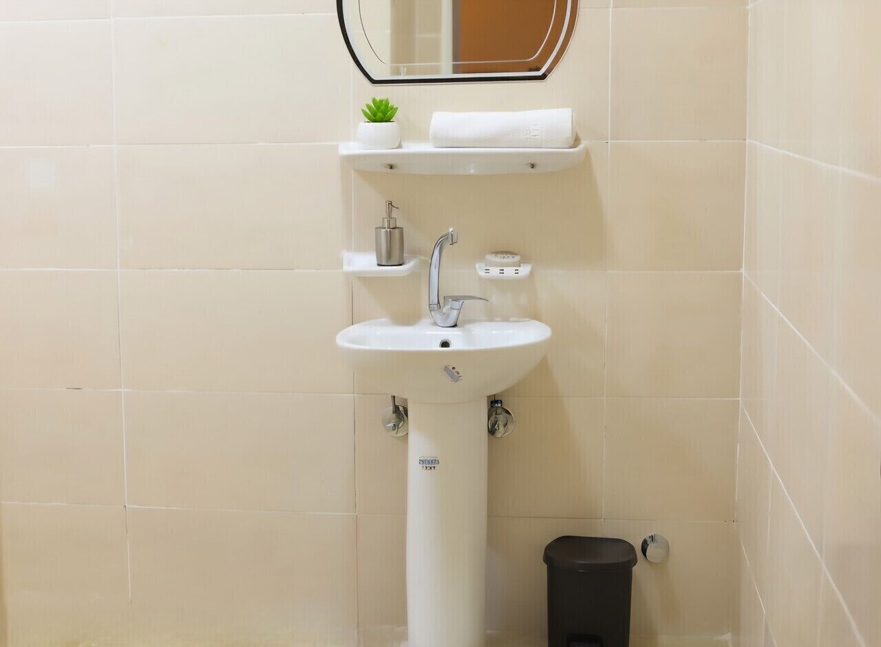 A bathroom with a white sink, a small shelf with a plant, a towel, and a trash bin.