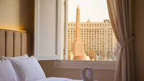 Ein Hotelzimmer mit Bett, einem Fenster mit Vorhängen und Blick auf ein Gebäude mit einem hohen Denkmal.