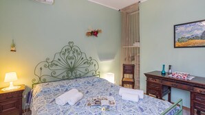 Un dormitori amb un llit, una taula de treball, una cadira, una làmpada i un quadre al mur.