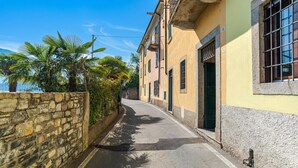 Un carrer estret amb parets de pedra, un edifici groc amb una porta verda i palmeres.