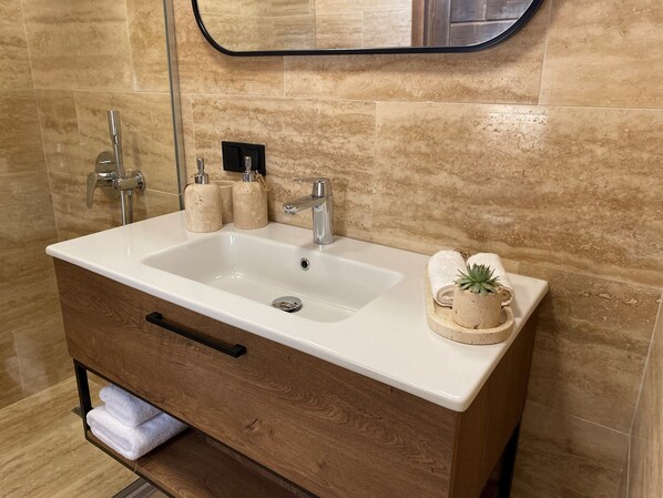 A bathroom with a white sink, two faucets, a wooden vanity, and a mirror above the sink. - Samadhi Alaçatı (Cesme)