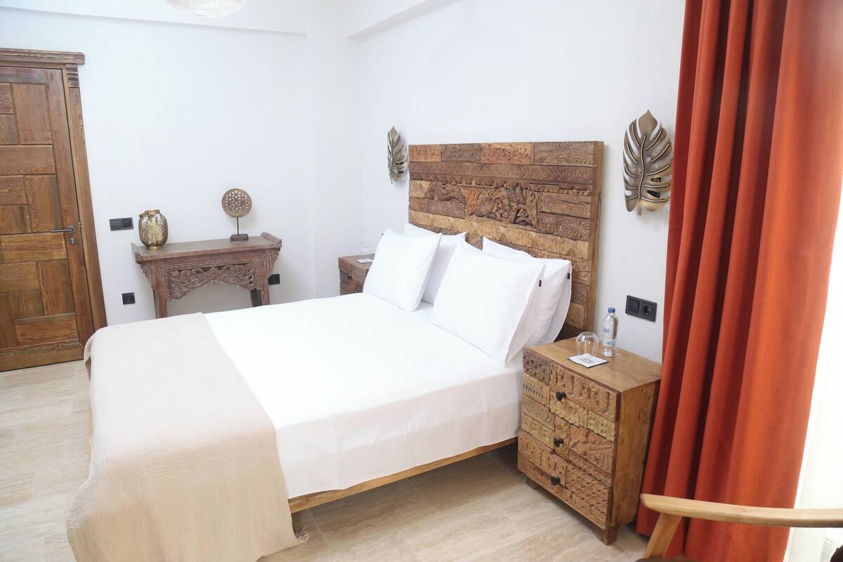 A bedroom with a wooden headboard, a wooden nightstand, a bedside table, and a wooden chest of drawers.