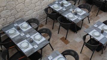 A restaurant with outdoor seating, stone walls, and neatly set tables with plates, cutlery, and glasses.