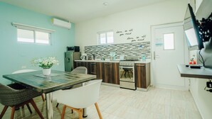 A modern kitchen with a dining area, featuring a kitchen island, white chairs, and a decorative wall with a love quote. - Comfortable and beautiful Suite (Oranjestad)