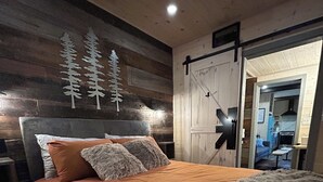 Et soveværelse med en stor seng, en sengegavl, en lampe på væggen og en dør, der fører til et andet rum.