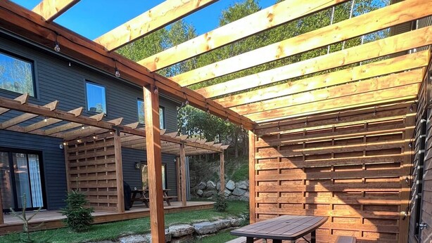 A wooden deck with a picnic table and benches, surrounded by a wooden pergola structure. - Modern 3-en-suite Bedroom Townhouse with 1 Sofa Bed and Terrace Mont-Tremblant (Mont-Tremblant)