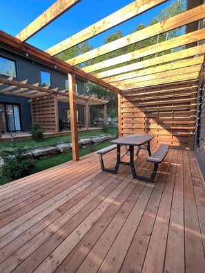 En træterrasse med et picnicbord og bænke, omgivet af en pergola i træ.