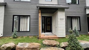 A two-story house with a grey siding exterior, a front porch, and a number '2223' on the door. - Modern 3-en-suite Bedroom Townhouse with 1 Sofa Bed and Terrace Mont-Tremblant (Mont-Tremblant)