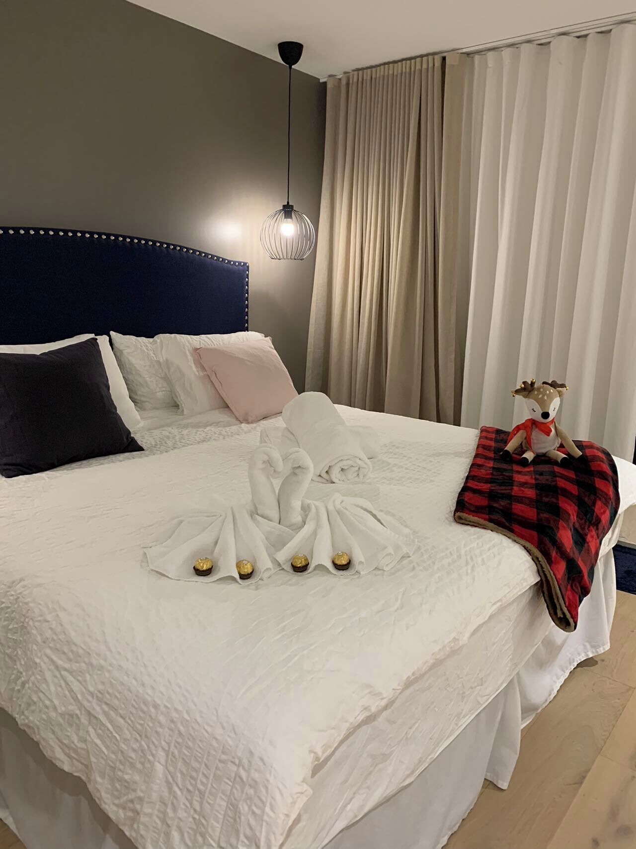 A neatly made bed with a white duvet, a decorative swan towel arrangement, and a plush toy on a red and black blanket.