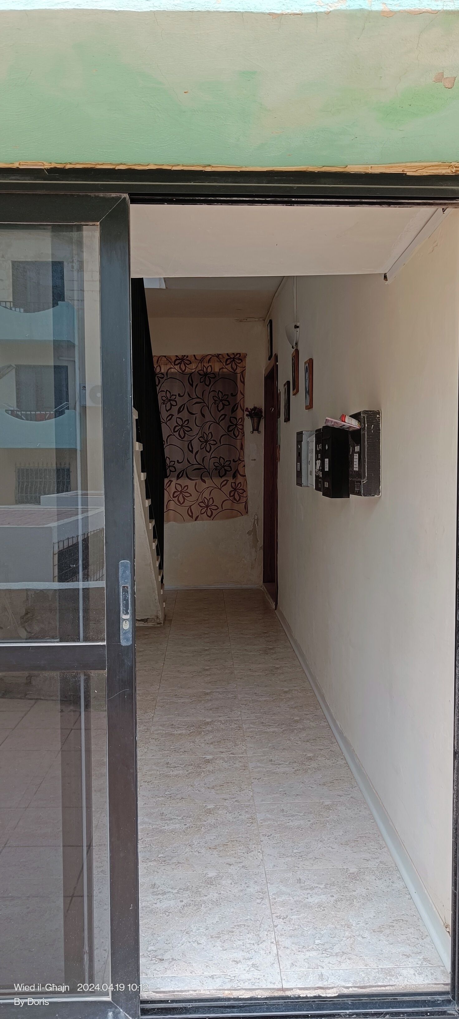 Un pasillo con piso de baldosas, una cortina estampada y una escalera que lleva a un nivel superior.