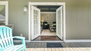 Een houten terras met een welkomstmat, een lichtblauwe Adirondack-stoel en een leren bank in de achtergrond.