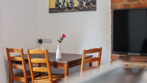 A dining area with a wooden table and chairs, a vase with a red flower, and a TV mounted on a brick wall. - Ideal for a Longer Stay or Contractor, Sleeps 1-4 (Cleckheaton)
